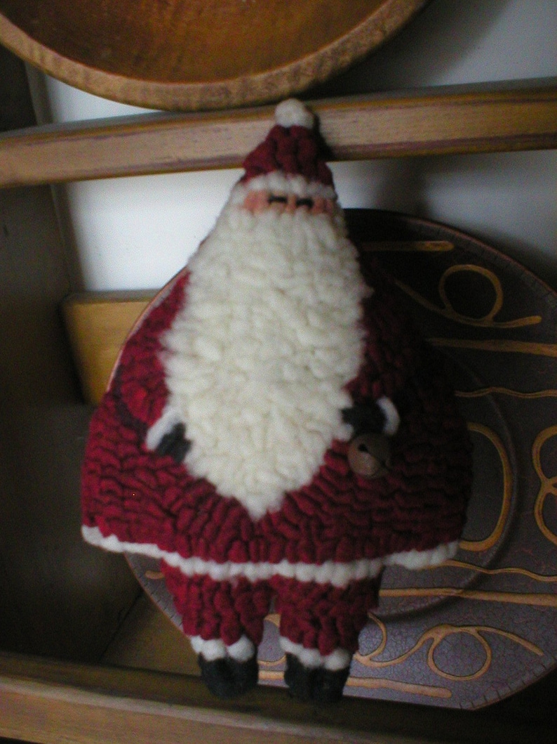 May include: A red and white felt Santa Claus ornament with a white beard and a red hat. The ornament is holding a small bell in its right hand.