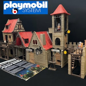 Könnte beinhalten: Ein Playmobil System Spielzeug-Burgset mit beigefarbenen, steintexturierten Wänden, roten Ziegeldächern, einem hohen Wachturm und mehreren Bogentüren. Zwei kleine Ritterfiguren sind innerhalb der Struktur platziert. Eine Anleitung liegt bei.