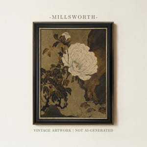 May include: A framed artwork titled MILLSWORTH featuring a large white peony flower with dark green leaves and a rock formation against a muted gold background. The rectangular print is enclosed in a black frame with a thin silver inner border.