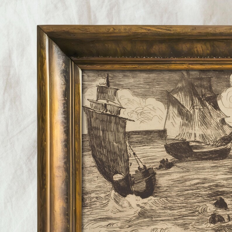 May include: A framed nautical etching depicts two sailing ships at sea. The artwork is in black and white, with detailed linework showing the waves and clouds. The frame is a warm gold color, adding a classic touch.