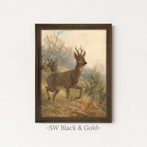 May include: A framed wall art print featuring an oil painting of a brown roe deer with antlers standing in a grassy field, with a second smaller deer visible in the background near bare trees, all enclosed in a dark brown textured frame.