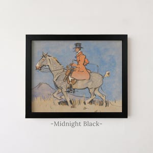 May include: A framed print featuring a watercolor illustration of a rider in a top hat and orange coat on a dappled grey horse against a blue sky and tan landscape. The black frame is labeled Midnight Black at the bottom of the image.
