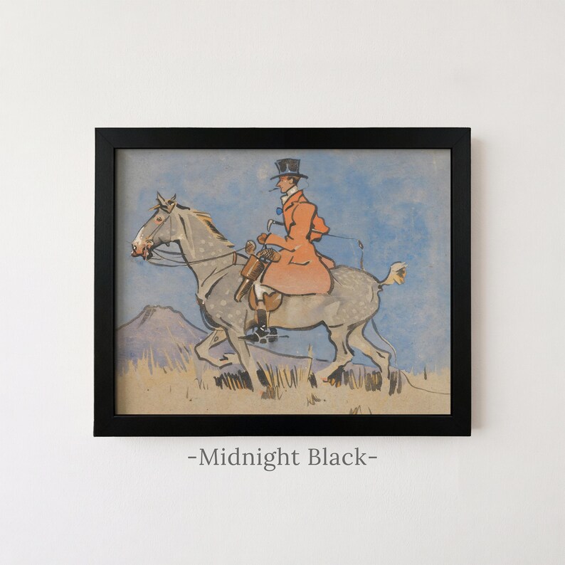 May include: A framed print featuring a watercolor illustration of a rider in a top hat and orange coat on a dappled grey horse against a blue sky and tan landscape. The black frame is labeled Midnight Black at the bottom of the image.