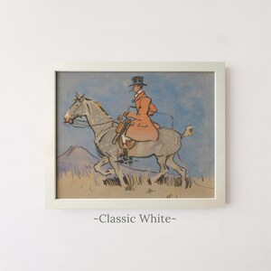 May include: A framed print featuring a watercolor illustration of a rider in a top hat and orange coat mounted on a dappled gray horse. The rider carries a crop and the scene is set against a blue sky and tan landscape. The frame is Classic White.