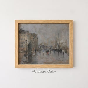 May include: A framed oil painting in a light-toned oak frame depicting a rainy harbor scene with muted gray and brown tones. The artwork shows buildings, ships, and small figures walking along a wet quay, with the text Classic Oak below.