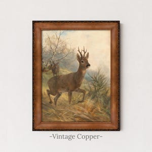 May include: A framed wall art print featuring a painting of a brown roe deer with antlers standing in a grassy field, with a second smaller deer visible in the background near bare trees, all enclosed in a dark brown decorative wooden frame.