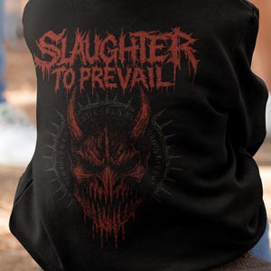 Könnte beinhalten: Schwarzer Kapuzenpullover mit dem roten Schriftzug "SLAUGHTER TO PREVAIL" und einer roten dämonischen Gesichts-Grafik. Der Pullover wird von einer Person getragen. Das Design befindet sich auf der Rückseite des Kleidungsstücks.