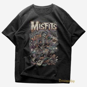 Peut inclure: T-shirt noir avec un graphisme d'un zombie jouant de la guitare, avec le nom du groupe "Misfits" dans une police vieillie. Le design comprend des crânes, des pierres tombales et les mots "Punk Flyer" et "Vintage Rockers."
