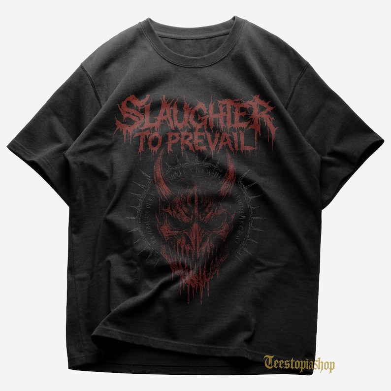 May include: Black t-shirt featuring the band name "Slaughter to Prevail" in red, dripping font above a red demonic face graphic. The design includes horns and a spiky circular border. The t-shirt has short sleeves and a crew neck.