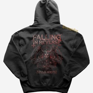 Może przedstawiać: Ciemnoszara bluza z kapturem z nazwą zespołu "Falling in Reverse" i napisem "Popular Monster" w kolorze czerwonym. Grafika na plecach przedstawia rogatego demona z pentagramem i innymi symbolami.