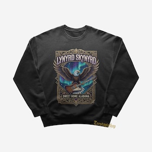 Pode incluir: Uma camisola preta de gola redonda com uma impressão gráfica de uma águia-de-cabeça-branca a segurar uma guitarra elétrica. O design inclui o texto Lynyrd Skynyrd e Sweet Home Alabama sobre um fundo de aurora boreal numa moldura dourada.