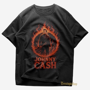 May include: Black t-shirt with a graphic of Johnny Cash within a ring of flames, holding a guitar. The name "JOHNNY CASH" is printed in red below the image. The shirt has a crew neck and short sleeves.