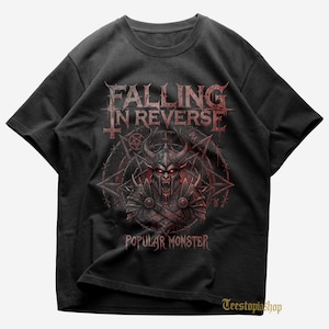 May include: Black t-shirt featuring the band name "Falling in Reverse" in a distressed, gothic font above a red illustration of a horned demon. The text "Popular Monster" is below the illustration. The design is encircled by a pentagram and other symbols.