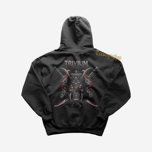 May include: Black hoodie featuring a graphic of a skull with samurai armor, crossed swords, and the band name "Trivium" in silver. The design includes red accents and is centered on the back of the hooded sweatshirt.