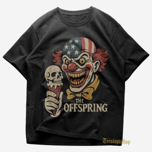 May include: Black t-shirt featuring a clown with an American flag design on its head, holding a skull-shaped ice cream cone. The text "THE OFFSPRING" is printed below the clown. The shirt has a crew neck.