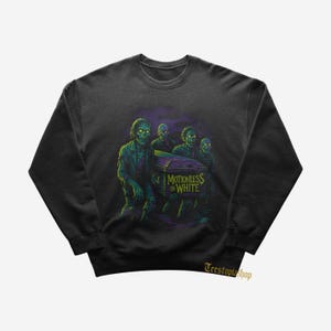 Może przedstawiać: Ciemnoszara bluza z grafiką zombie niosących trumnę. Na trumnie widnieje napis "Motionless in White". Zombie są zielone i żółte, na fioletowo-zielonym tle.