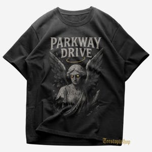 Puede incluir: Camiseta negra con el nombre de la banda "Parkway Drive" sobre una ilustración de una estatua de ángel con alas y un halo. El ángel tiene ojos amarillos. La camiseta tiene cuello redondo.