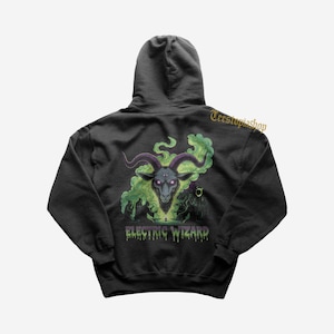 May include: Black hoodie featuring a graphic of a goat head with purple horns and glowing eyes, surrounded by green smoke. The text "ELECTRIC WIZARD" is below the image. The hoodie has a hood and a relaxed fit.