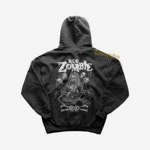May include: Black hooded sweatshirt featuring a white graphic of Rob Zombie with skulls, a pentagram, and the text "ROB ZOMBIE". The design is centered on the back of the sweatshirt.