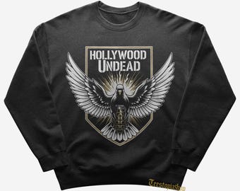 Könnte beinhalten: Dunkelgraues Sweatshirt mit einer Grafik einer Taube mit ausgebreiteten Flügeln, einem Granatenkörper und dem Text "HOLLYWOOD UNDEAD" in einem Schilddesign. Das Design ist in Weiß- und Goldtönen gehalten.