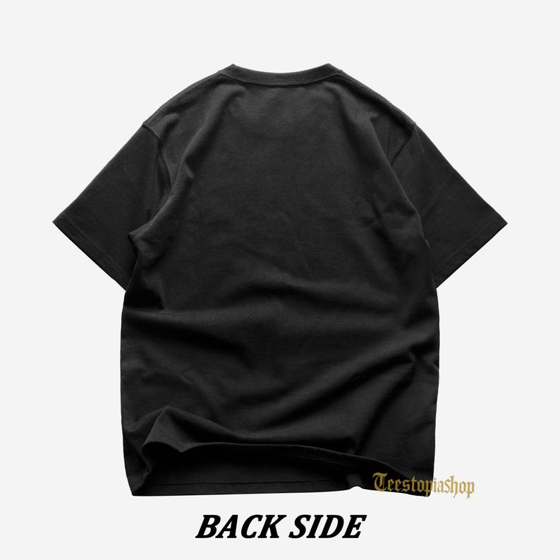 Puede incluir: Camiseta negra de manga corta con el texto "BACK SIDE" en letras blancas en negrita en la parte inferior. La camiseta se muestra sobre un fondo blanco. El nombre de la marca "Teestoriashop" est&aacute; impreso en dorado en el lado derecho.