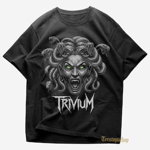 May include: Black t-shirt featuring a Medusa graphic with snakes for hair, green eyes, and an open mouth. The word "TRIVIUM" is printed in white, stylized lettering below the graphic. The shirt is a crew neck.