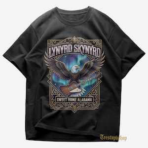 May include: Black t-shirt featuring a graphic of an eagle with outstretched wings, holding a guitar. The design includes the text "LYNYRD SKYNYRD" and "SWEET HOME ALABAMA" in a decorative frame, with a colorful aurora borealis background.