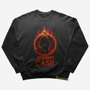May include: Dark gray sweatshirt featuring a graphic of Johnny Cash inside a ring of flames. The image shows Cash holding a guitar, with the name "JOHNNY CASH" in red block letters below. The sweatshirt is a crew neck style.