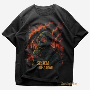 May include: Black t-shirt featuring a person in a gas mask with a red and orange industrial background. The text "SYSTEM OF A DOWN" is printed in gold. The shirt has a crew neck.