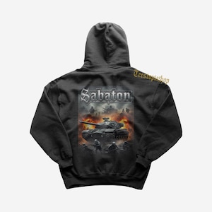 Puede incluir: Sudadera con capucha negra con un gráfico de un tanque en una escena de guerra. El diseño presenta el nombre de la banda "Sabaton" en una fuente gótica plateada, junto con soldados y explosiones, creando una imagen dinámica y llena de acción.