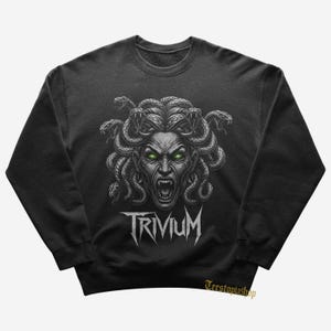 May include: Dark gray sweatshirt featuring a Medusa graphic with snakes for hair and glowing green eyes. The word "TRIVIUM" is printed in white below the graphic. The sweatshirt is a crew neck style.