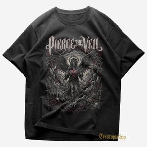 Può includere: T-shirt nera con la scritta "Pierce the Veil" sopra un'illustrazione gotica. La grafica raffigura un angelo che tiene un cuore, circondato da ali, nuvole e dettagli ornamentali. Girocollo.