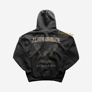 May include: Black hooded sweatshirt featuring the text "ALTER BRIDGE" above a graphic of a bird with outstretched wings, and the word "BLACKBIRD" below. The sweatshirt is a dark gray color.