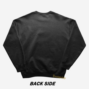 May include: A dark gray sweatshirt with the text "BACK SIDE" in bold, black letters at the bottom. The words "Teestoviashop" are in gold script on the lower right. The sweatshirt is a solid color with a crew neck and long sleeves.