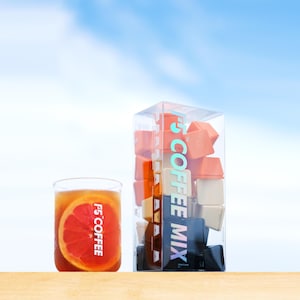 May include: A glass of iced tea with a grapefruit slice and a clear box of coffee mix cubes. The box has the text "F5 COFFEE MIX" in a vertical design. The glass also has the text "F5 COFFEE". The background is a bright blue sky.