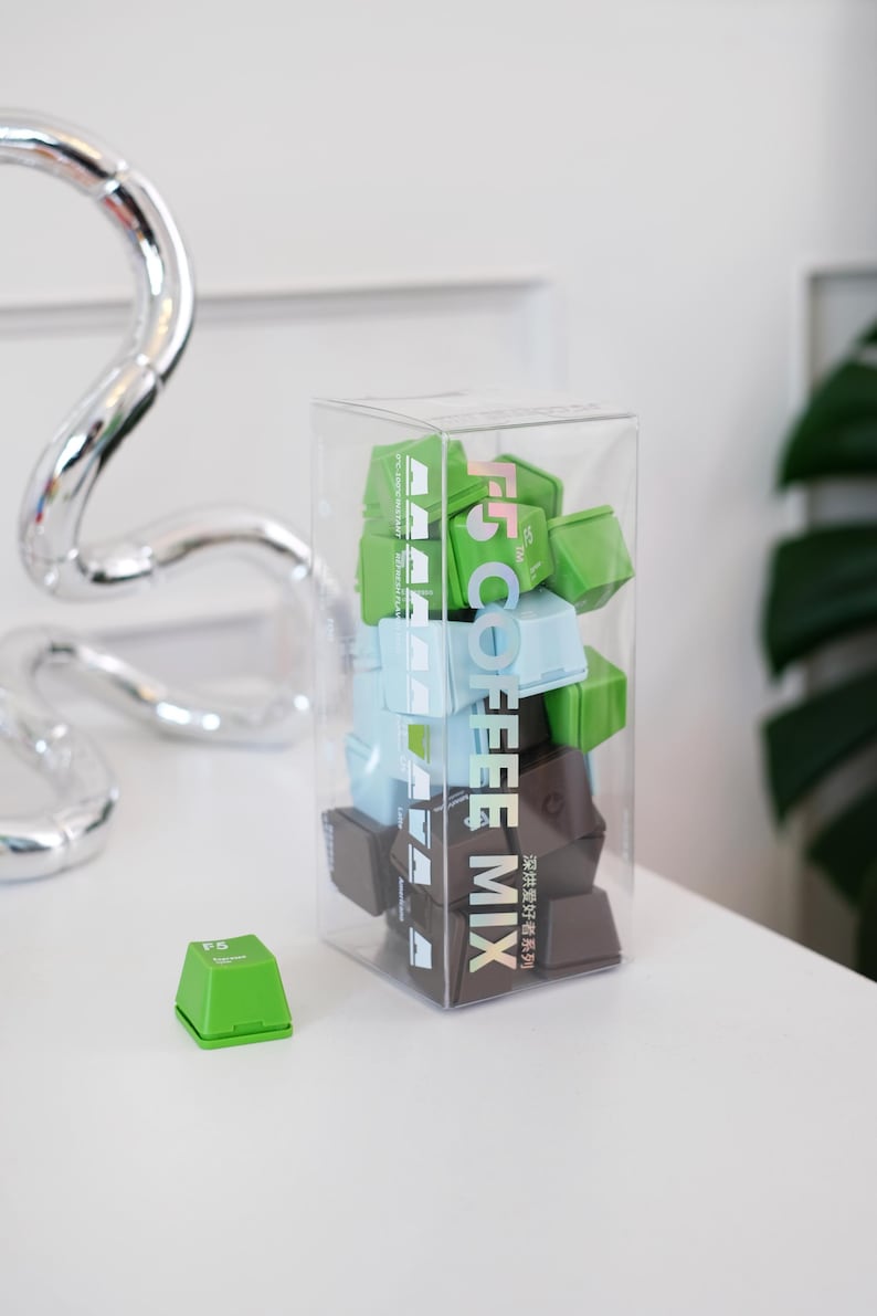Pu&ograve; includere: Una scatola trasparente piena di cubetti di miscela di caff&egrave; verdi, blu e marroni. Il testo "F5 COFFEE MIX" &egrave; stampato verticalmente sulla scatola. Un singolo cubo verde &egrave; su una superficie bianca.