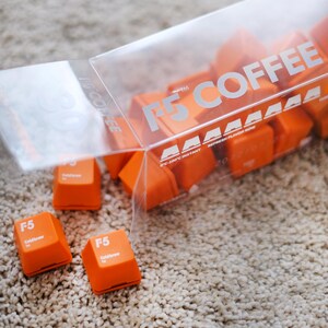 May include: Orange F5 Coldbrew coffee cubes spilling from a clear plastic container. The container has the text "F5 COFFEE" printed on it. The cubes are scattered on a beige carpet.