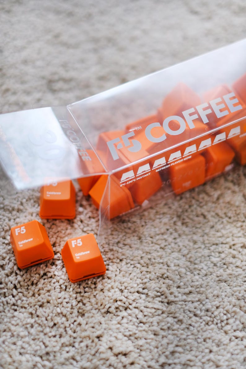 May include: Orange F5 Coldbrew coffee cubes spilling from a clear plastic container. The container has the text "F5 COFFEE" printed on it. The cubes are scattered on a beige carpet.