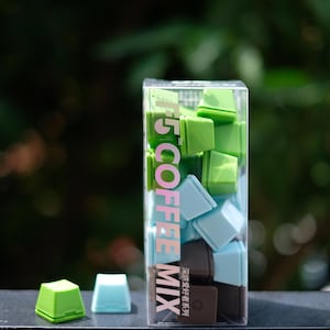Pu&ograve; includere: Una scatola trasparente piena di cubetti di miscela di caff&egrave; quadrati e colorati, nei toni del verde, blu e marrone. La scatola ha la scritta "T5 COFFEE MIX". Due cubetti sono fuori dalla scatola.