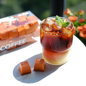 May include: A refreshing iced coffee drink with a sprig of mint, served in a clear glass. Beside it are two orange-colored, square-shaped candies and a box of similar candies. The box has the text "F5 COFFEE".