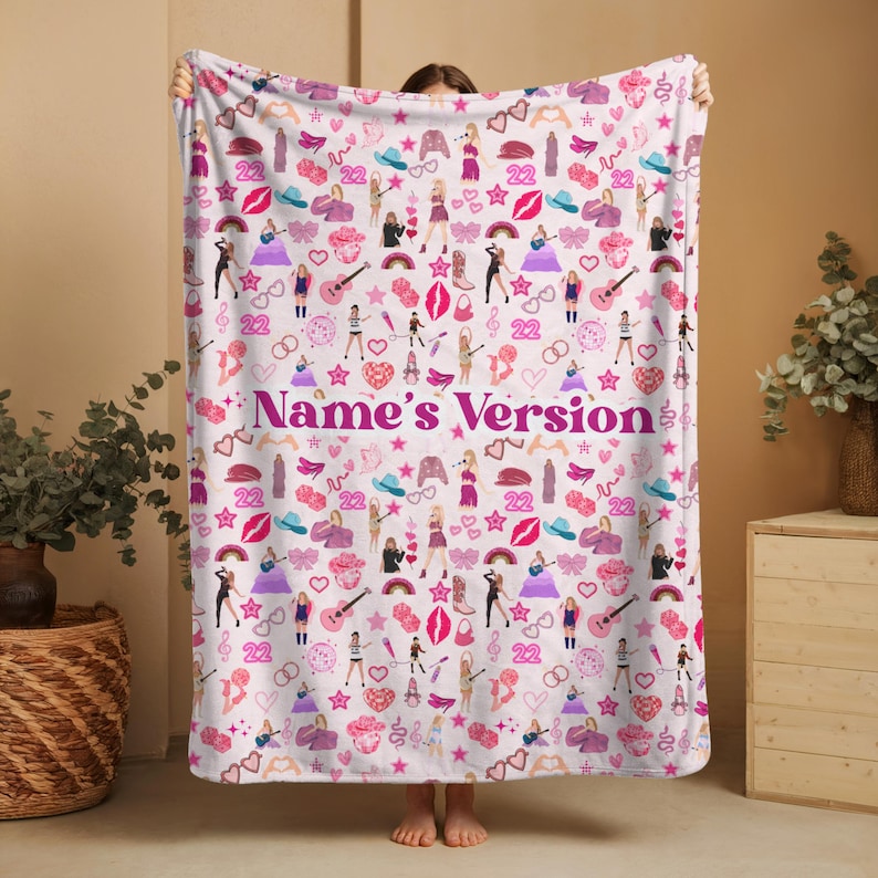 May include: A white blanket with a repeating pattern of pink and purple illustrations, including guitars, lips, and figures. The text "Name's Version" is displayed in a cursive font across the center of the blanket.