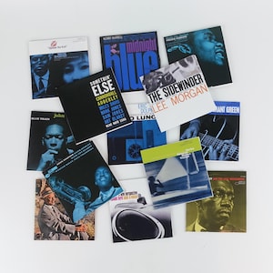 Può includere: Una collezione di copertine di album jazz vintage, con artisti iconici e titoli di album. Le copertine mostrano una varietà di colori, tra cui blu, nero e bianco, con ritratti e design grafici. I titoli includono "Midnight Blue" e "The Sidewinder."