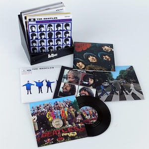 May include: A selection of The Beatles vinyl records and album covers, including "A Hard Day's Night," "Let It Be," and "Abbey Road." The records are displayed with a black storage box. The album covers feature images of the band members.