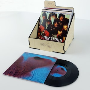 May include: A wooden record crate holding vinyl records, with the Pink Floyd album cover visible. A single record and its sleeve are in front of the crate. The sleeve has a blue and red design. The crate has the text "mini crate".