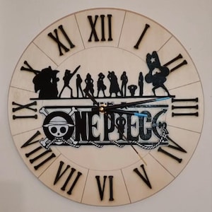 Può includere: Un orologio rotondo in legno con un quadrante beige chiaro e numeri romani neri. L'orologio presenta una silhouette nera di personaggi e la scritta "ONE PIECE" con un teschio e ossa incrociate.