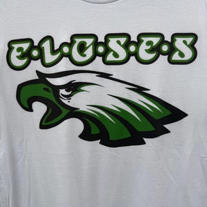 May include: White t-shirt with a green and black eagle graphic and the text "E.L.G.S.E.S."