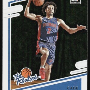 May include: A basketball trading card featuring Cade Cunningham of the Detroit Pistons. Cunningham is wearing a blue and red jersey and shorts, holding a basketball. The card has the Donruss logo and "The Rookies" text.