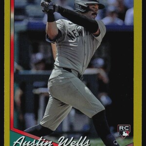 May include: A Topps baseball trading card featuring Austin Wells of the New York Yankees in a gray uniform, swinging a bat. The card has a gold border, a rookie card RC logo, and the text Austin Wells, YANKEES, and Topps printed on the front.