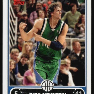 May include: A Topps trading card featuring Dirk Nowitzki of the Dallas Mavericks. The card has a blue border with the team name at the top. Nowitzki is in his green and blue Mavericks uniform, with the number 41 visible. The Topps logo is in the upper left corner.