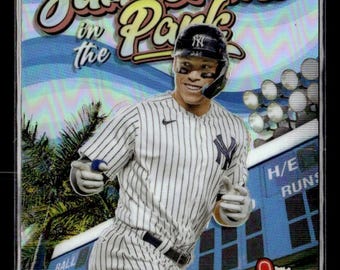 May include: A baseball card featuring Aaron Judge of the New York Yankees. The card has a holographic background with the words "Summertime in the Park." Judge is wearing a pinstripe uniform and helmet. A hot dog and foam finger are in the corner.